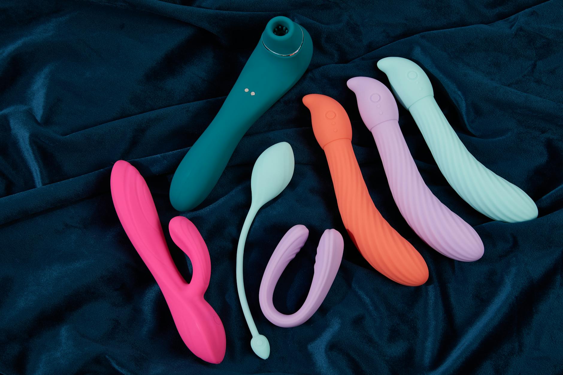 Array of silicone clitoral vibrators in various colors displayed on blue fabric