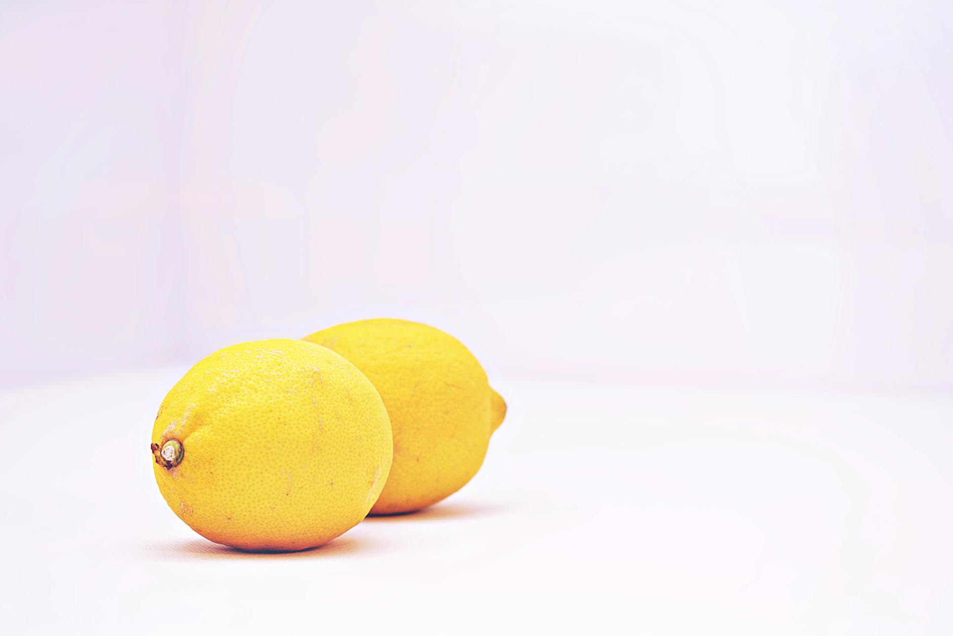 Two vibrant lemons placed against a minimalistic white background, showcasing freshness and simplicity.