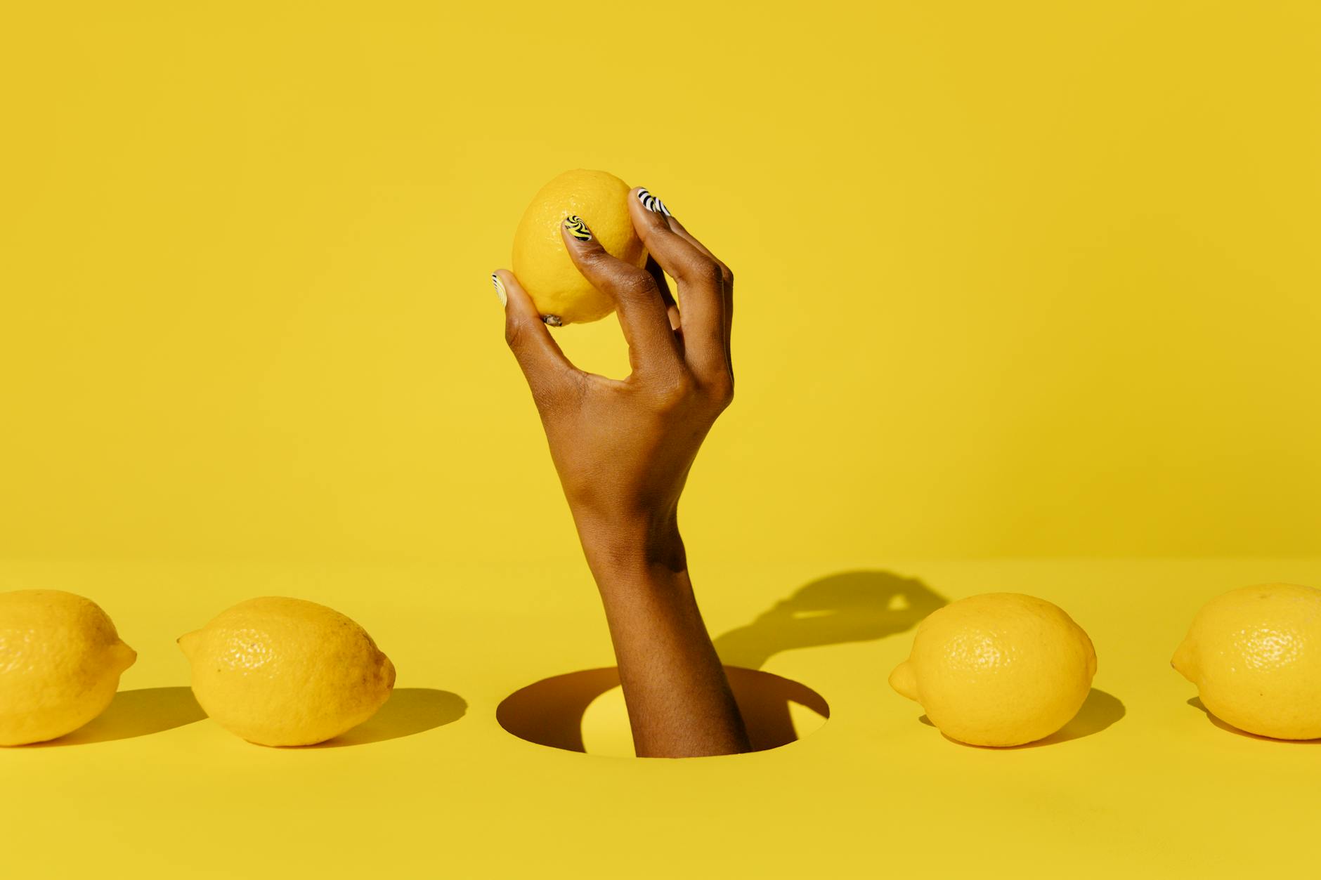 A hand holding a fresh lemon against a vivid yellow background, symbolizing the bright, modern design of lemon clitoral vibrators