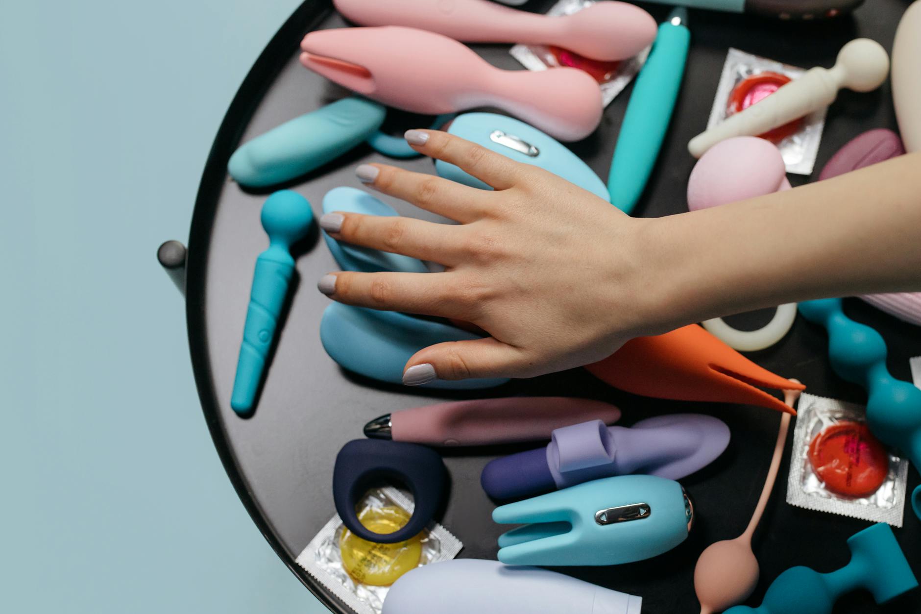 A hand reaching over a variety of colorful lemon clitoral vibrators arranged on a table