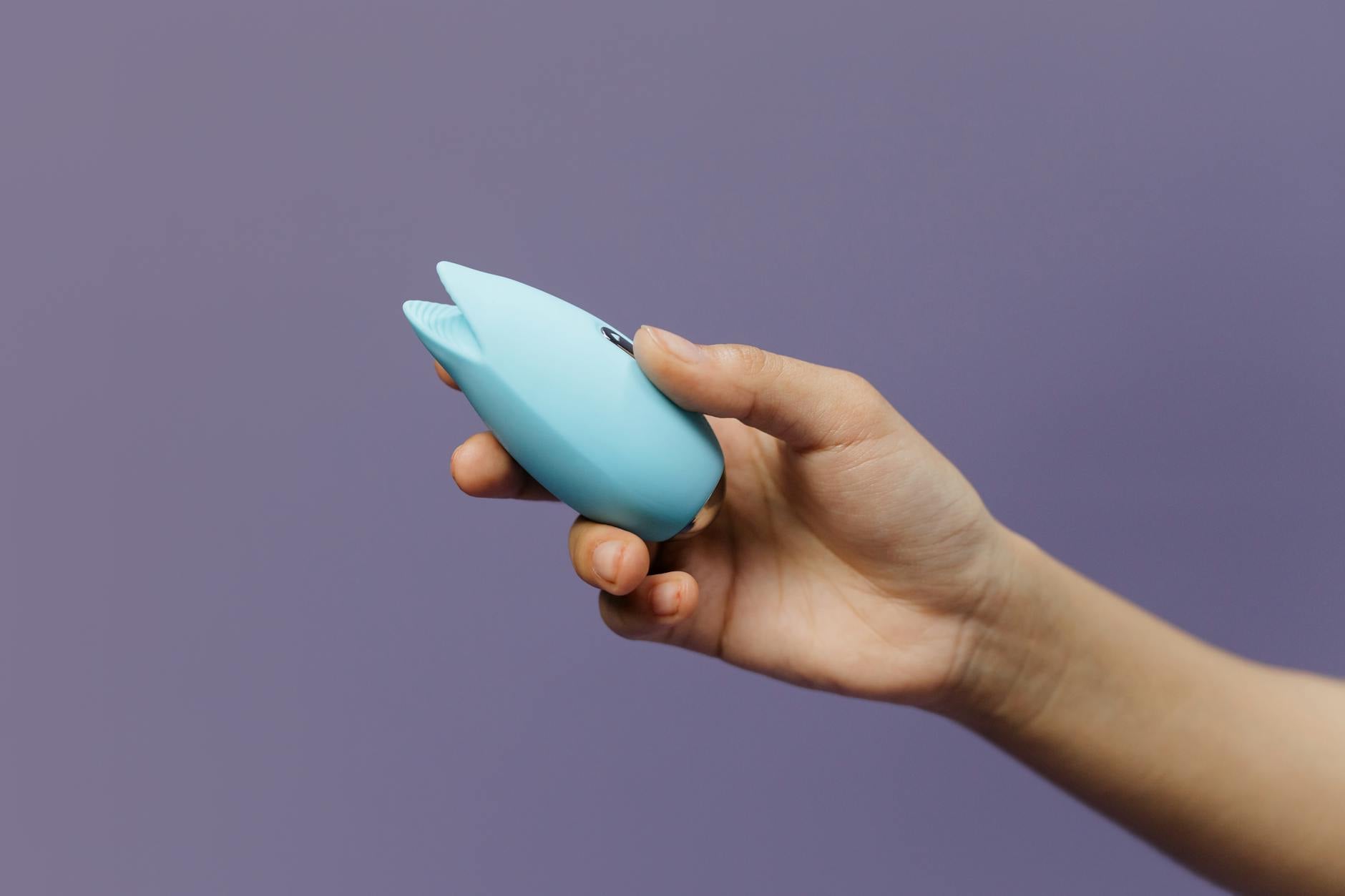 A silicone lemon clitoral vibrator held against a purple background
