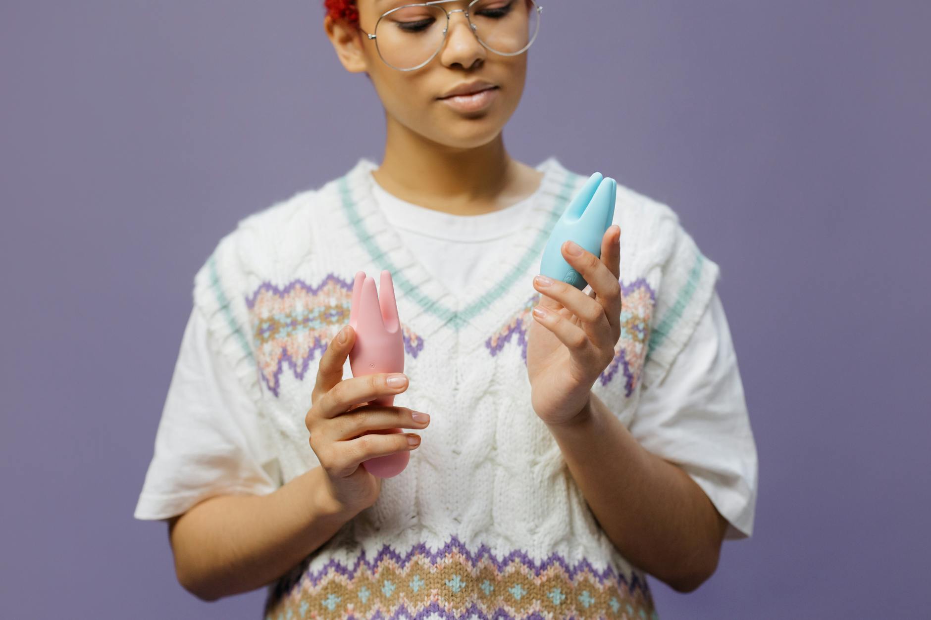 Woman holding blue and pink silicone vibrators with intentional, contemplative expression